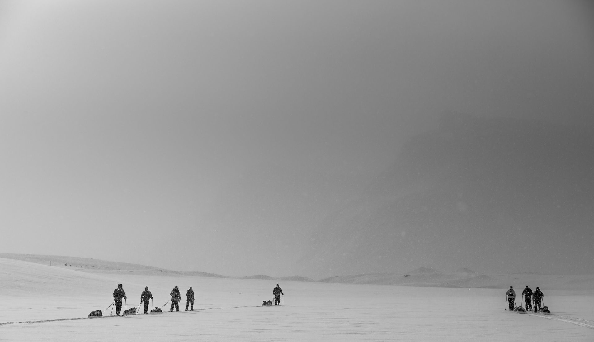 Grupo de expedicionarios cruzando un paisaje ártico con esquís y pulka en plena nevada