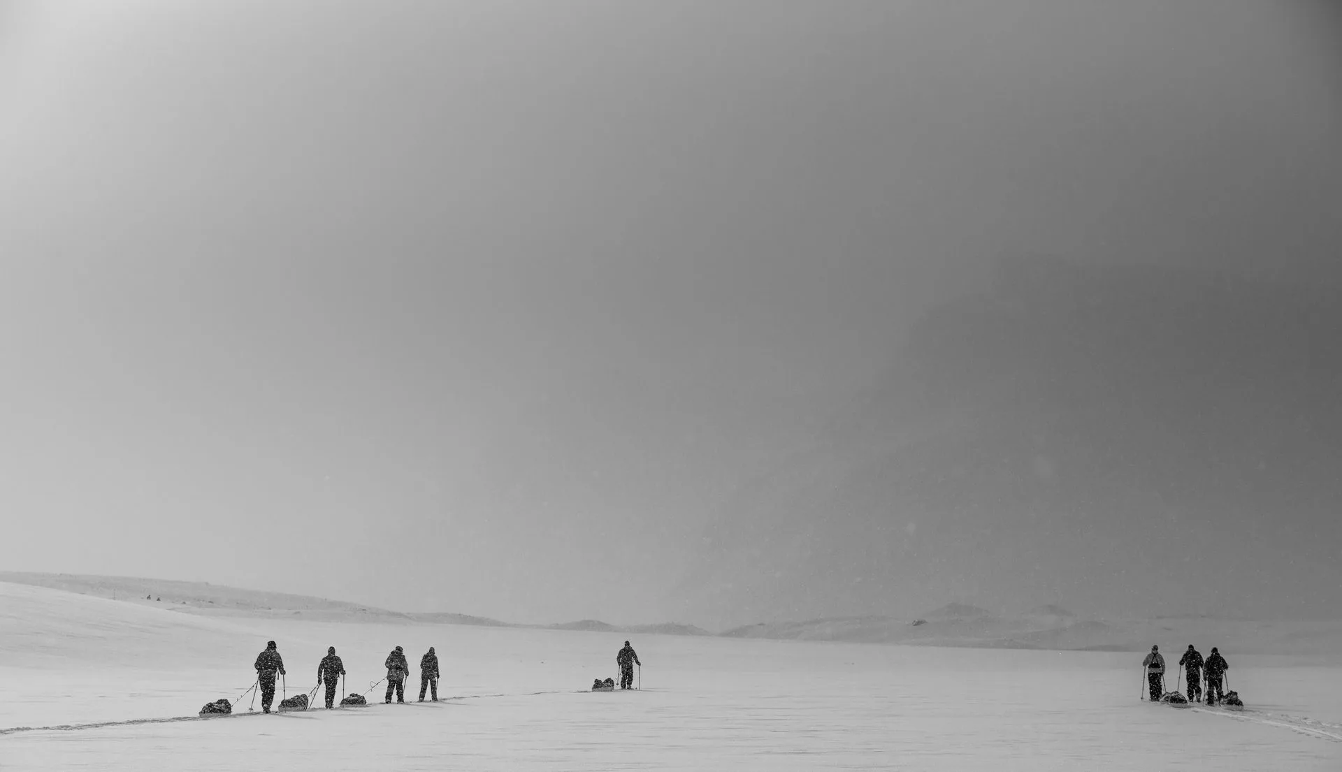 Grupo cruzando un paisaje ártico con esquís y pulka en plena nevada